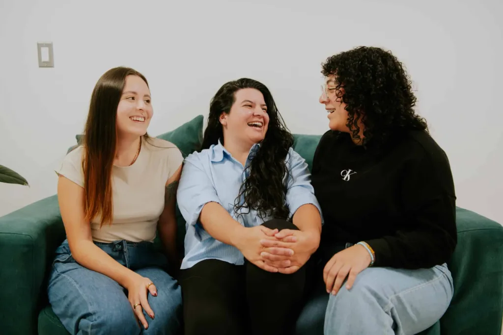 Tres integrantes del equipo de KIKU conversan y ríen sentadas en un sofá verde