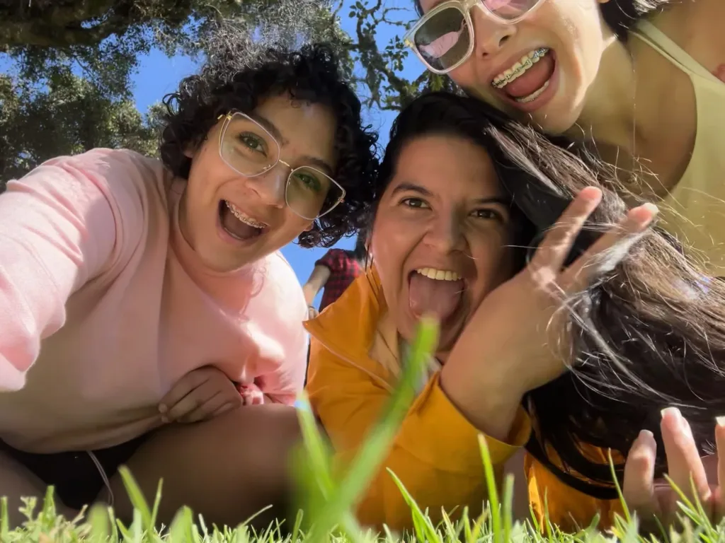 Tres integrantes del equipo de KIKU recostadas sobre el pasto en un selfie bajo un árbol